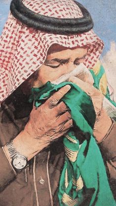 an old man with a green scarf is looking at his cell phone while wearing a headscarf