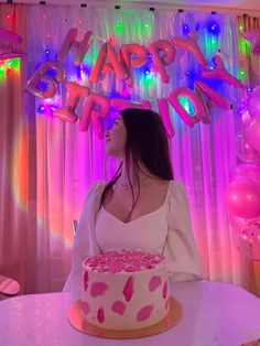 a woman sitting at a table with a cake in front of her and balloons behind her