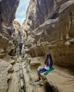 a woman sitting on top of a rock formation next to a narrow river filled with water