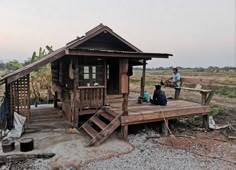 a person sitting on a wooden bench in front of a small house with stairs leading up to it