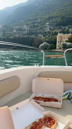 two pizzas in boxes sitting on the back of a boat