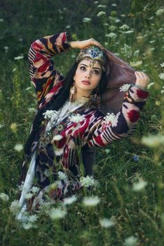 a woman is sitting in the grass with her hands on her head and looking at the camera