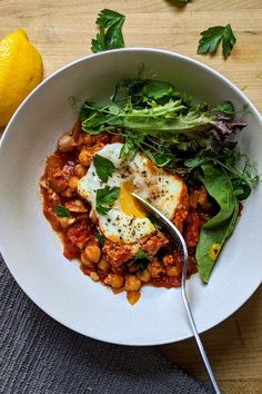 a white bowl filled with food next to a lemon and green leafy garnish