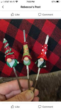 someone is holding three miniature christmas gnomes on toothpicks