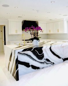 a large kitchen with marble counter tops and white cabinets, along with purple flowers in a vase on the island