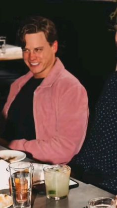 two men sitting at a table with plates of food and drinks in front of them