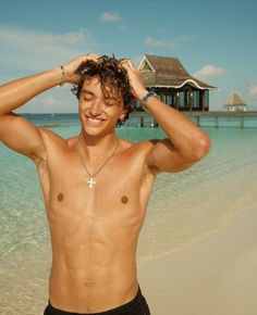 a man standing on top of a beach next to the ocean holding his hair up