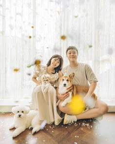 a man and woman are sitting on the floor with their two dogs in front of them