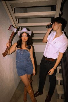 a man and woman dressed up as cowboys, one holding an ax while the other is talking on a cell phone