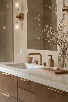 a bathroom sink sitting under a mirror next to a vase with flowers on top of it