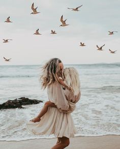 a woman walking on the beach with birds in the sky above her and holding onto her back