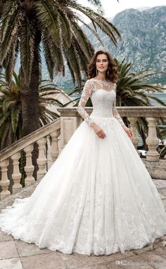 a woman in a wedding dress standing on a balcony with palm trees and mountains behind her