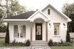 a small white house with two windows and brick walkway leading to the front door area