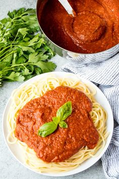 a plate of spaghetti with sauce and parsley next to a pot of tomato sauce