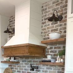 a kitchen with brick walls and wooden shelves above the stove top, along with two hanging lights