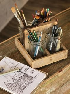 a wooden box filled with pencils and other art supplies on top of a table