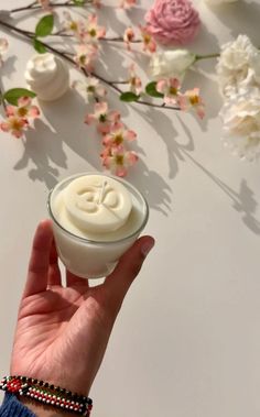 a hand is holding a small candle in front of some pink and white flowered branches