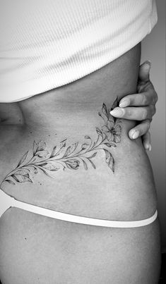 a woman's stomach with flowers and leaves tattooed on the bottom part of her belly