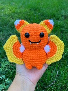 a hand holding an orange and yellow crocheted stuffed animal with wings on it