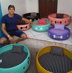 a man sitting on the ground next to several dog beds that are in different colors