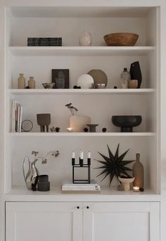 a white bookcase filled with lots of books next to a vase and candle holder