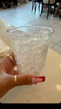 a hand holding a glass filled with ice and water on top of a white counter