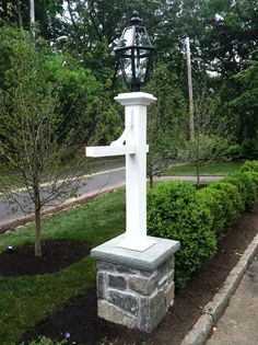 a large white cross sitting in the middle of a garden next to a sidewalk and trees