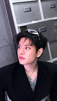 a young man with black hair and glasses on his head sitting in front of filing cabinets