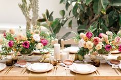 the table is set with white plates and pink flowers in vases on each plate