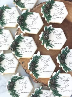 cookies decorated with pine cones and greenery are arranged on a wooden platter that has the names of their guests