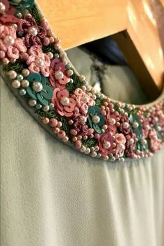 a close up of a dress with flowers and pearls on the collar, hanging from a wooden hanger