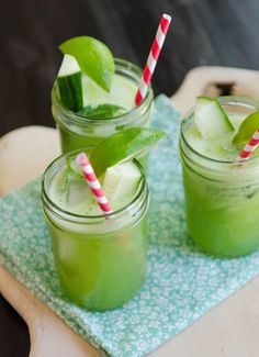 two mason jars filled with green drinks on top of a cutting board