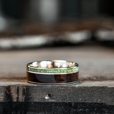 two wedding bands with green and white glitters on them sitting on a piece of wood