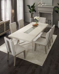 a dining room table with white chairs and a rug on the floor in front of it