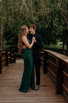 a man and woman standing on a bridge in front of trees holding each other's hands