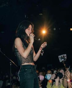 a woman standing in front of a crowd holding a microphone and singing into a mic