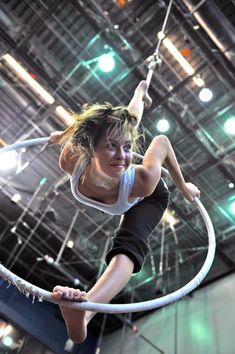 a woman is doing aerial tricks on a rope in an indoor area with lights overhead