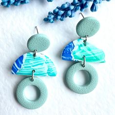 two pairs of earrings with blue and green designs on them sitting next to some flowers