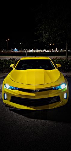 a yellow sports car parked in a parking lot at night with its lights on and the hood up