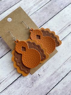 three brown and tan leather earrings on top of a piece of cardboard next to a card