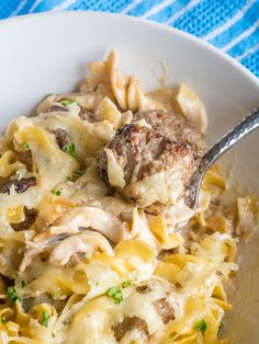 a white bowl filled with pasta and meat covered in cheese sauce on top of a blue table cloth