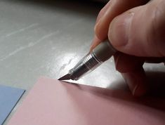 a person is writing on a piece of pink paper with a pen in their hand