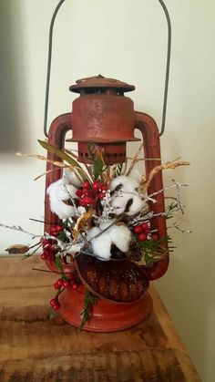 an old fashioned lantern with cotton and berries in it sitting on a wooden table next to a wall