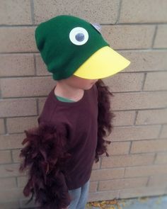 a young child wearing a green and yellow duck hat standing in front of a brick wall