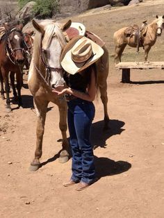 a woman standing next to a brown horse wearing a cowboy hat