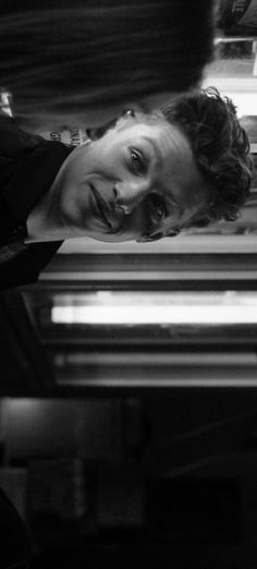 black and white photograph of a woman leaning over an oven door looking at the camera