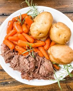 a white plate topped with meat, potatoes and carrots on top of a wooden table