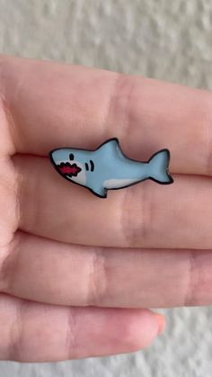 a hand holding a small blue and white shark pin