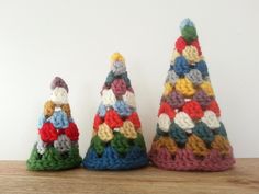 three crocheted christmas trees sitting on top of a wooden table