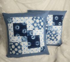 two blue and white decorative pillows sitting on top of a bed next to each other